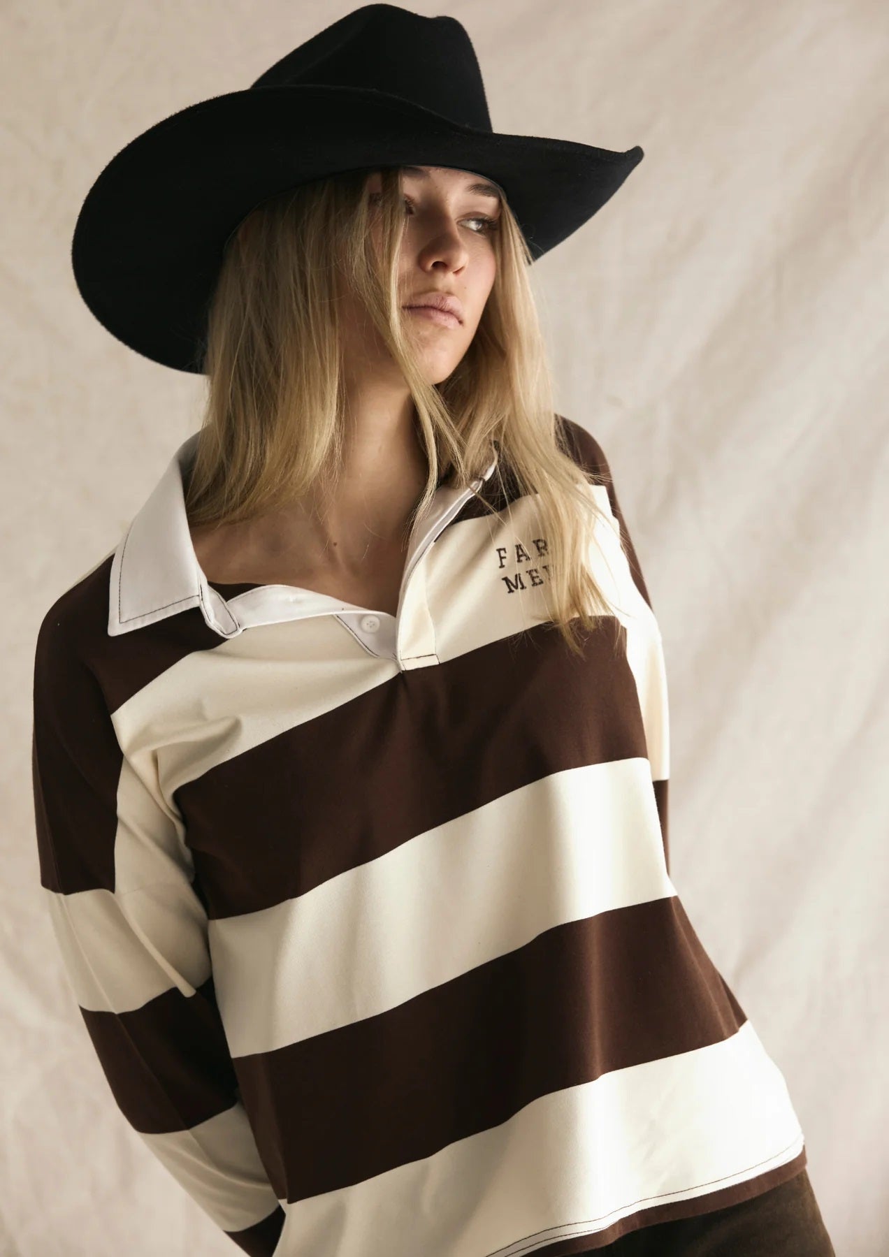 Person wearing a black and white striped shirt with a logo and a black cowboy hat on a plain background