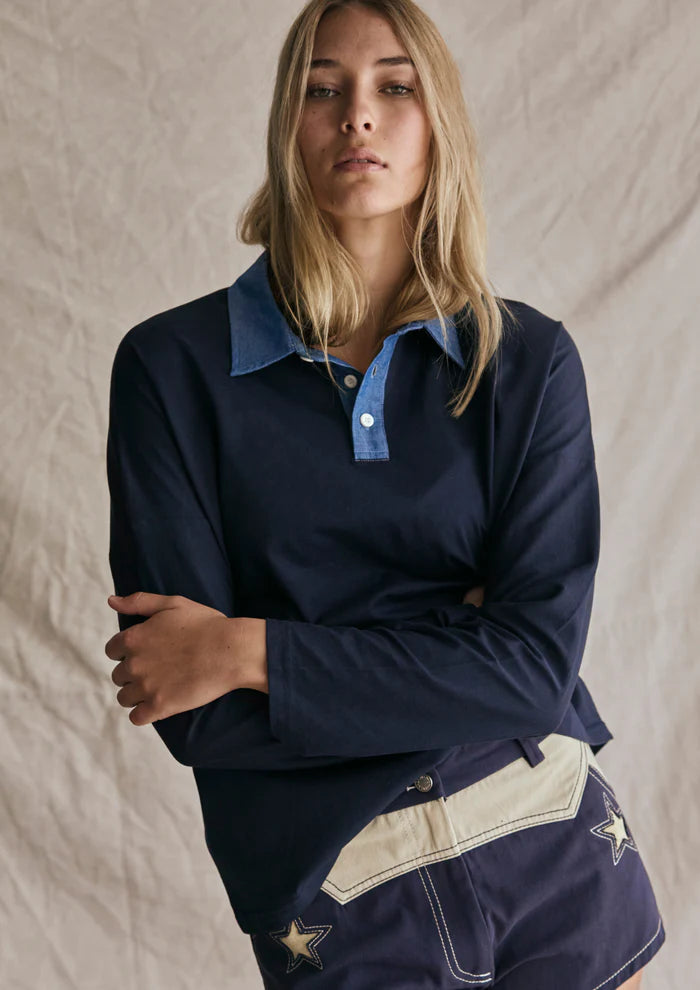 Person wearing a navy long-sleeve shirt with a collar and shorts on a beige background
